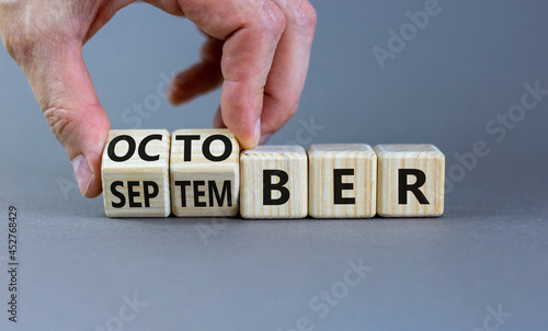 Symbol for the change from September to october. Businessman turns wooden cubes and changes the word 'September' to 'October'. Beautiful grey background, copy space. Happy October concept.