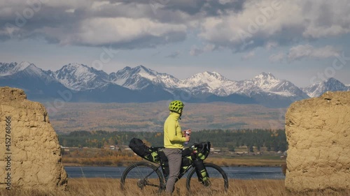 The man travel on mixed terrain cycle touring with bikepacking. The traveler journey with bicycle bags. Sport bikepacking, bike, sportswear in green black colors. Mountain snow capped, stone arch. photo