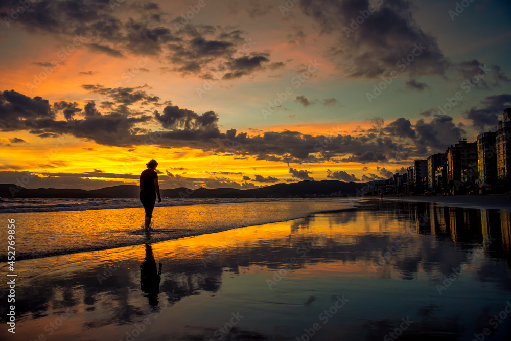 Pessoa caminha ao nascer do sol laranja com lindo reflexo em Itapema - Paisagem natural