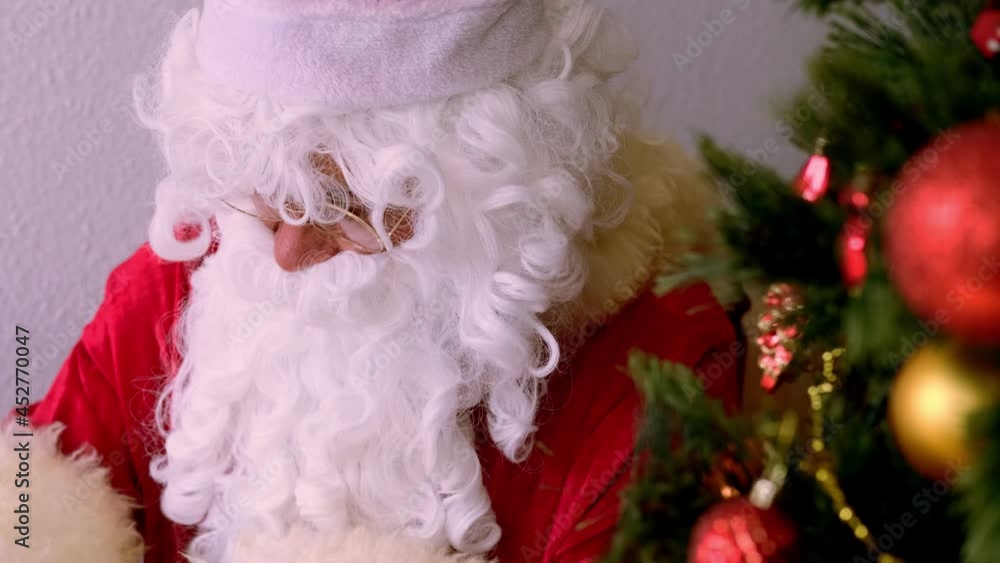 Santa claus in a traditional red costume with a white beard sits near a decorated Christmas tree, boxes with gifts, wishes happy new year, concept of congratulations, wishes, merry christmas Santa claus in a traditional red costume with a white beard sits near a decorated Christmas tree, boxes with gifts, wishes happy new year, concept of congratulations, wishes, merry christmas