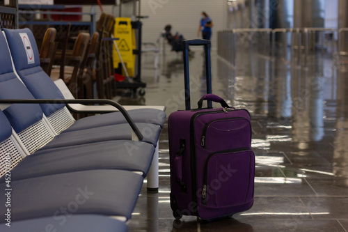 Unattended small carry on lugagge by empty bench seats at airport terminal. Purple suitcase left alone, security hazard concepts photo