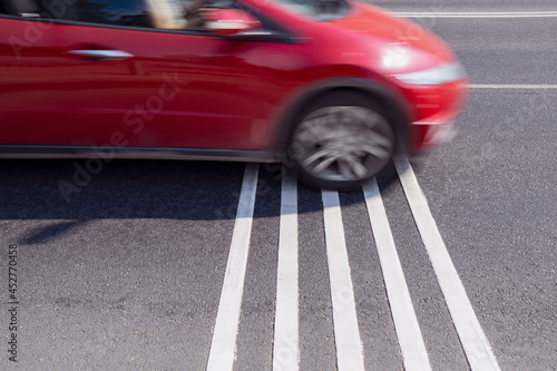 Rumble strips or speed breakers on asphalt road surface and red car crossing them in motion blur. Traffic calming concept.