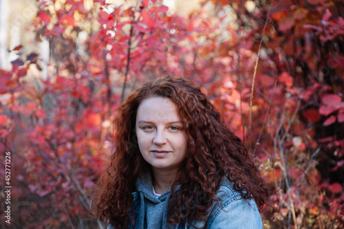 woman portrait close up. woman with long curvy brown hair in autumn forest with red bush on background. 