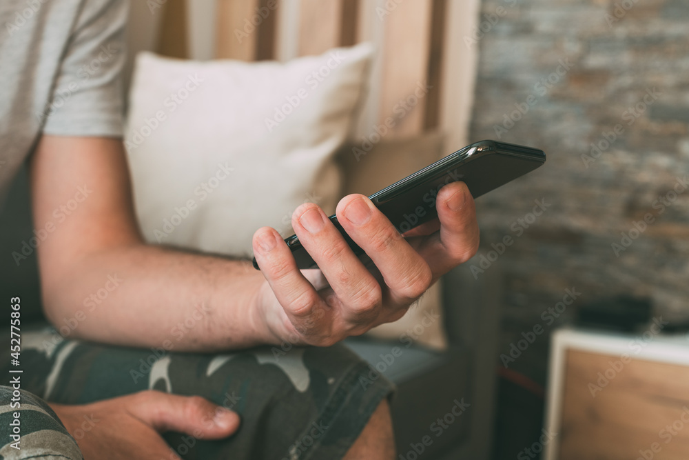 Obraz premium Close up of casual male hands using mobile smart phone at home in privacy of his living room