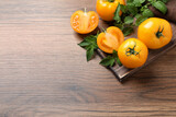 Fresh ripe yellow tomatoes with leaves on wooden table, flat lay. Space for text