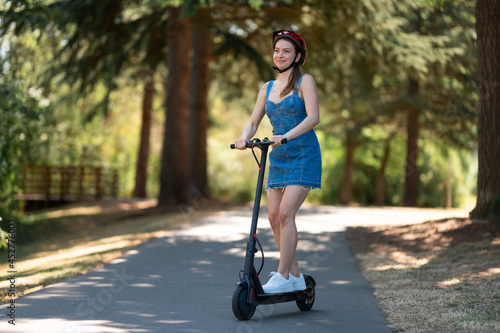 A girl in a protective helmet rides in the park on a bicycle path on an electric scooter. Sunny day, beautiful nature. There are no people around. New technologies, environmentally friendly transport.