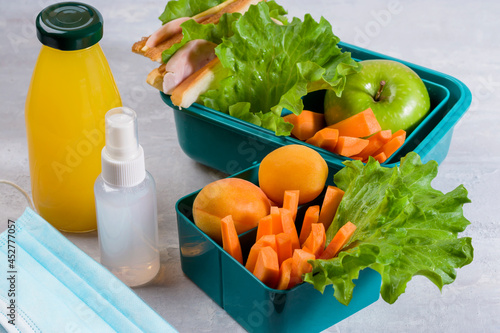 Delicious school lunch. Hygiene and protection against bacteria and viruses. Lunch box with a sandwich, fresh vegetables and fruits, a bottle of juice on a light background. Zero waste concept.