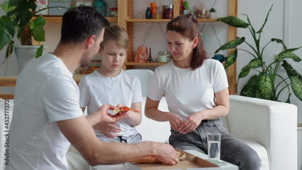 Family takeaway food at home. Spbi Bearded father gives slices of delicious hot pizza to joyful wife and little son and family enjoys weekend sitting on sofa Family takeaway food at home. Spbi Bearded father gives slices of delicious hot pizza to joyful wife and little son and family enjoys weekend sitting on sofa