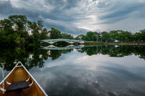 Fototapeta Naklejka Na Ścianę i Meble -  A bridge over a pond n the Toronto Islands, shot from a canoe on the water with late afternoon clouds reflected int he still waters.