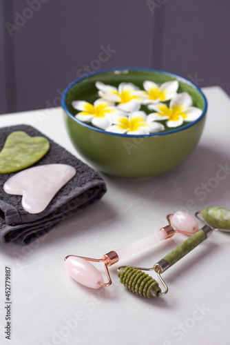 Beautiful spa composition with plumeria flowers. Face roller and guasha massager. Chinese Gua Sha massage tools.