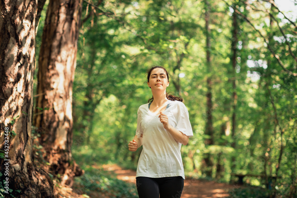 Portrait of young woman in sports clothes is jogging at summer forest. The concept of cross-country running and wellness