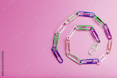 A chain of multi-colored paper clips on a pink background