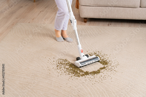 Young woman uses cordless vacuum cleaner to clean home carpet. Close-up of mung bean brush from carpet.