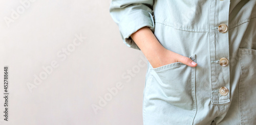 Close-up of a woman's hand in a large pocket of a working cotton light green jumpsuit with large buttons. Eco-style, natural clothing for work and home