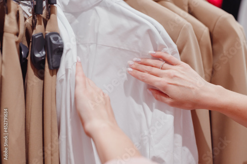 Woman shopping in fashion mall  choosing new clothes  looking through hangers with different casual colorful garments on hangers  close up of hands