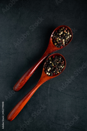Wooden spoon with a mix of pepper on black background. Dried aromatic spice.