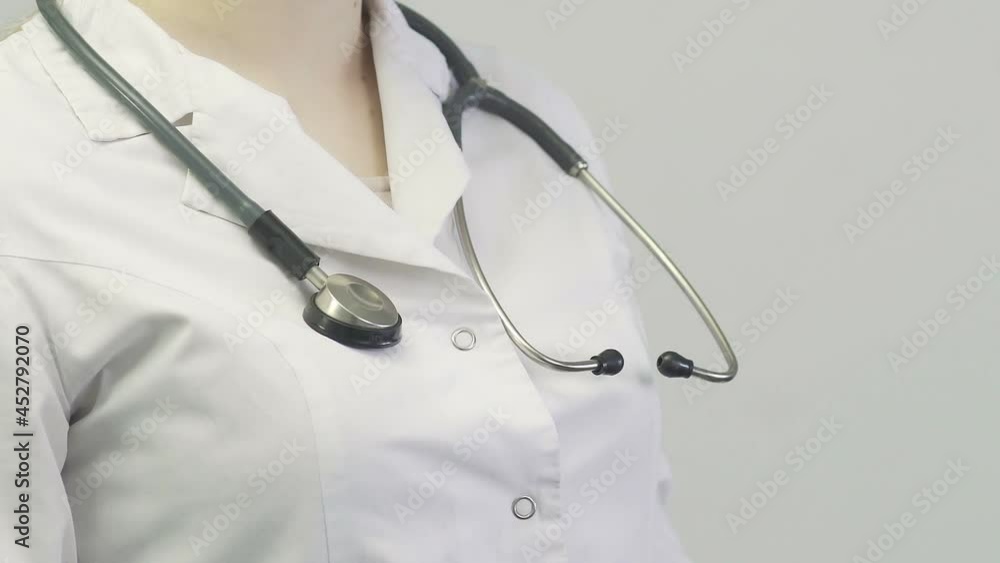 Close-up of a doctor a woman in a medical gown puts a stethoscope on her neck Close-up of a doctor a woman in a medical gown puts a stethoscope on her neck