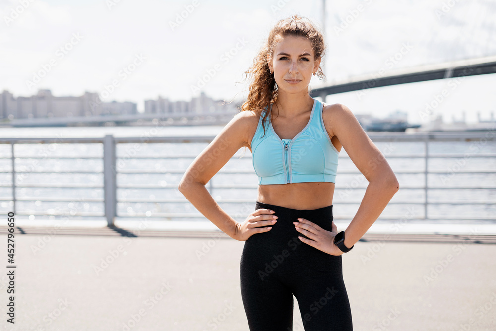 A sporty woman does exercises in the open air. Healthy lifestyle, sports activities in the city. The trainer is engaged in fitness on the street. A smart watch on your hand for counting calories.