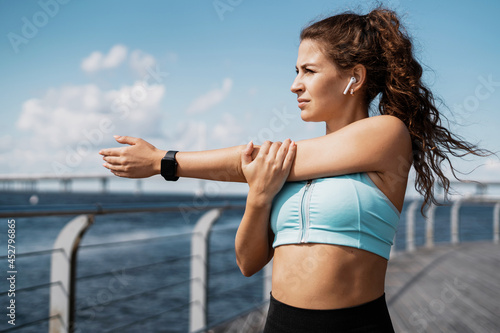 The trainer is engaged in fitness on the street. A smart watch on your hand for counting calories.A sporty woman does exercises in the open air. Healthy lifestyle, sports activities in the city.