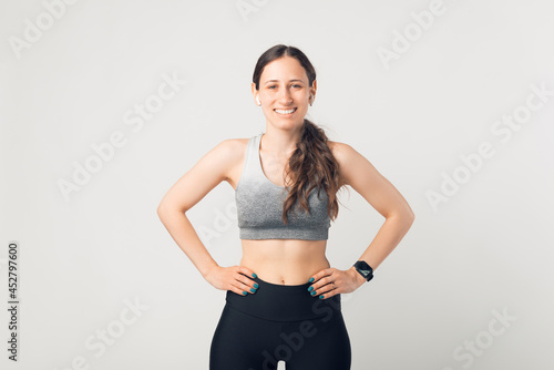 Portrait of a young sporty woman smiling at the camera with the hands on her hips. © Vulp