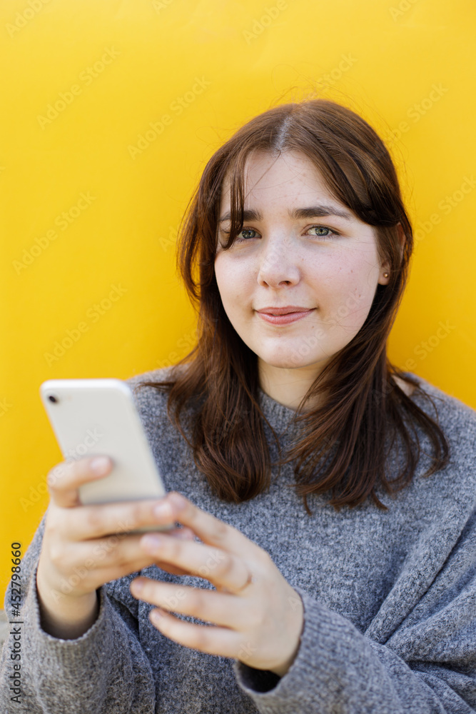 Woman using mobile phone next to the yellow background. Social media screen. Clubhouse the voice-only social media app. Clubhouse, a social platform built around drop-in audio chat. Using social app Woman using mobile phone next to the yellow background. Social media screen. Clubhouse the voice-only social media app. Clubhouse, a social platform built around drop-in audio chat. Using social app