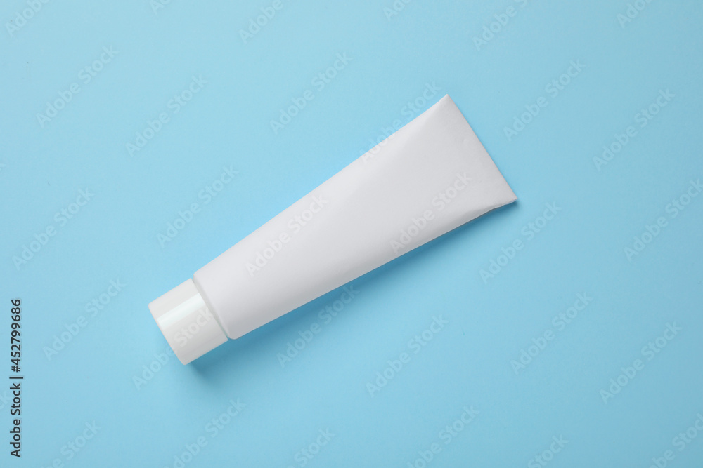 Blank tube of toothpaste on light blue background, top view