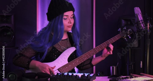 Medium shot of female bass player rehearsing before the gig in a small club playing a musical instrument on stage performing live. Photoshoot of beautiful music artist backstage posing for press kit