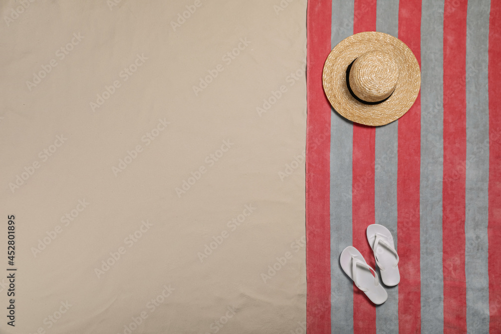 Beach towel, flip flops and hat on sand, top view. Space for text Beach towel, flip flops and hat on sand, top view. Space for text