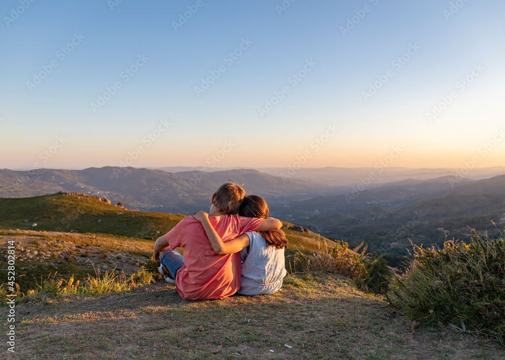 miúdos a apreciar paisagem ao por-do-sol na montanha