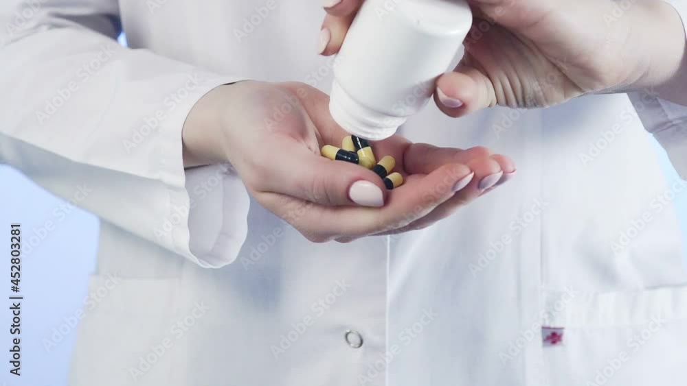 Close-up of an unrecognizable woman, a doctor, holding a jar of pills and throwing it into her hand Close-up of an unrecognizable woman, a doctor, holding a jar of pills and throwing it into her hand