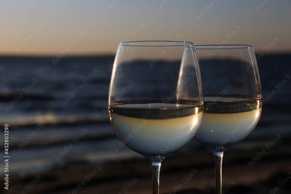 Two glasses of wine near river at sunset, closeup. Space for text