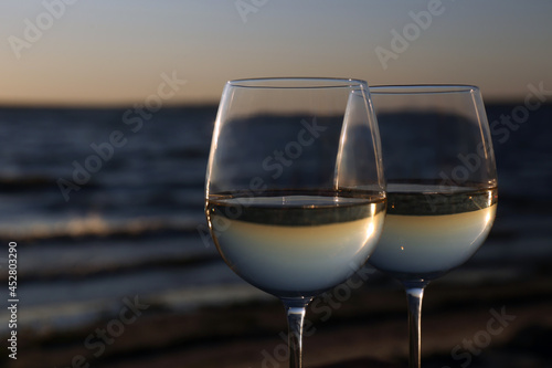 Two glasses of wine near river at sunset, closeup. Space for text