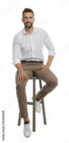 Handsome man sitting on stool against white background photo