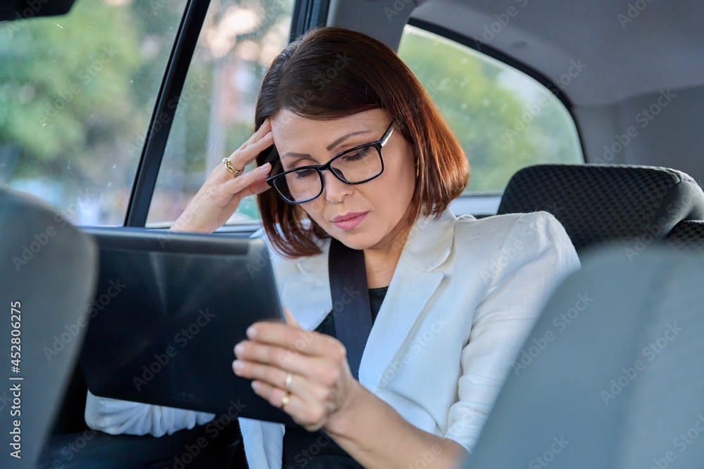 Serious middle-aged business woman in car in passenger backseat. Serious middle-aged business woman in car in passenger backseat.