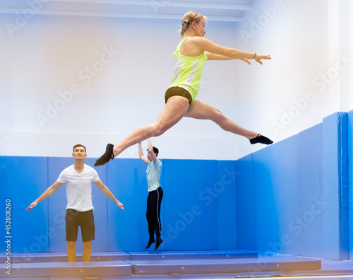 Young athletic woman exercising acrobatic elements in jump on trampoline in sports center.. © JackF