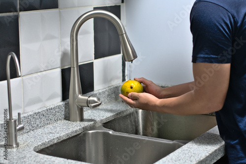 Man washing a mango in the kitchen sink