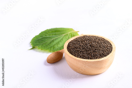 Perilla seeds in a wooden bowl with spoon and perilla leaf on white background, Healthy herbal seed ingredients in Asian food