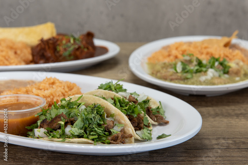 Variety of plates on the table with the carne asada tacos flavored with cilantro and onion featured up front