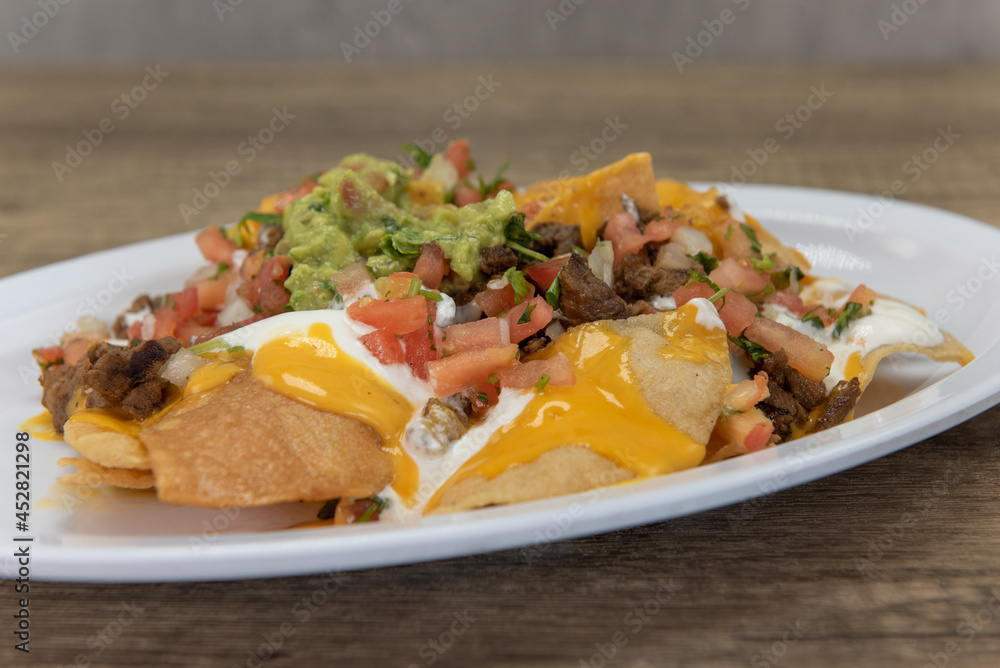 Hearty plate of nachos smothered with melted cheese, pico de gallo, and sour cream to serve as a meal
