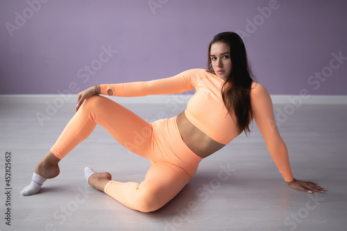 Beautiful slender woman in a sports overalls is engaged in stretching 