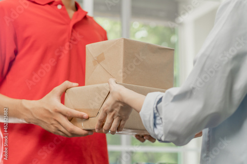 Delivery, asian young man, male postman holding cardboard box parcel, carton or mail in red uniform send to client, customer woman received from messenger, Service business, shopping online.