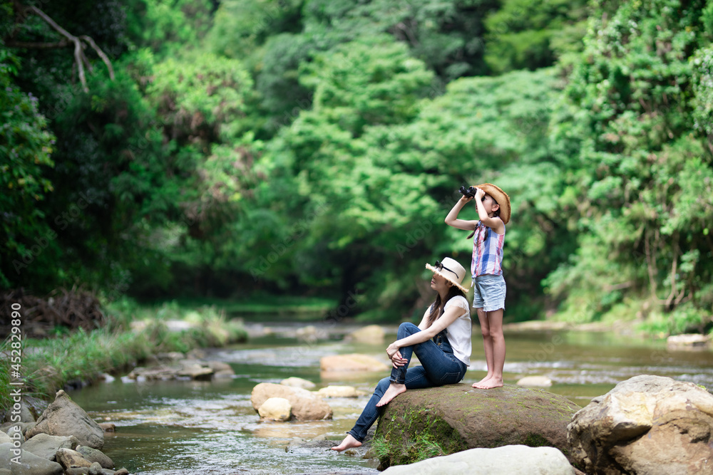 Obraz premium 渓流の岩の上で双眼鏡を使う母と娘