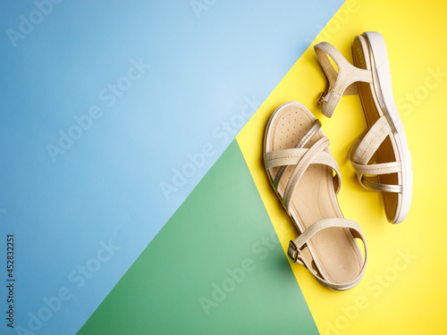 Stylish beige leather summer comfortable women's sandals on bright yellow, green and blue paper background. Concept of recreation by sea and summer vacation. Flat lay, top view, copy space. photo