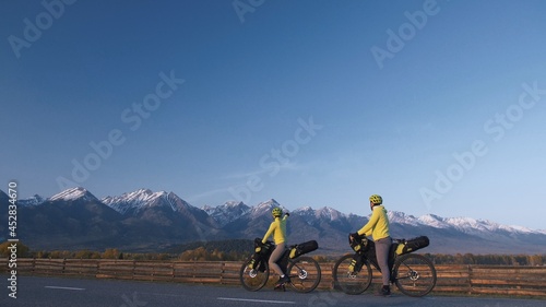 The man and woman travel on mixed terrain cycle touring with bikepacking. The love couple journey with tent in nature with bicycle bags. Stylish bikepacking, bike, sportswear in green black colors. photo