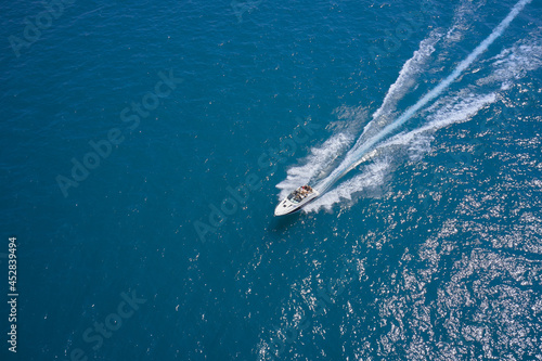 Large white boat on the water in motion top view. Luxury motor boat on dark blue water aerial view. Speedboat with people fast moving on dark water. Travel on high-speed boats on the water.