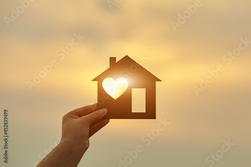 Woman holding a wooden house in front of the sun
