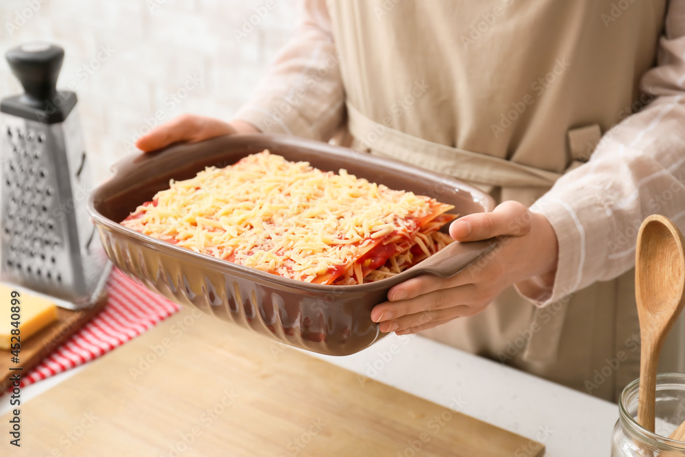 Woman holding baking dish with tasty tomato lasagna at table in kitchen, closeup Woman holding baking dish with tasty tomato lasagna at table in kitchen, closeup