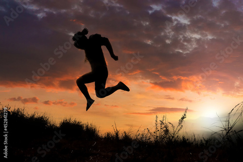 Silhouettes of men jumping with joy and freedom In the meadow during the evening time. man jump high and step on the sun in the silhouette.