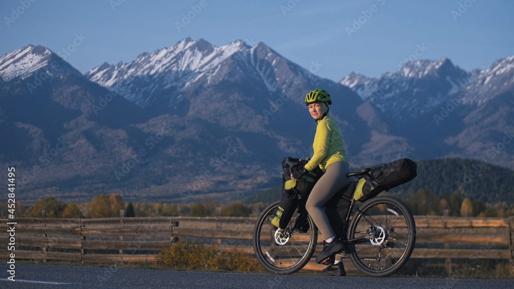 Fototapeta premium The woman travel on mixed terrain cycle touring with bikepacking. The traveler journey with bicycle bags. Sport tourism bikepacking, bike, sportswear in green black colors. Mountain snow capped.
