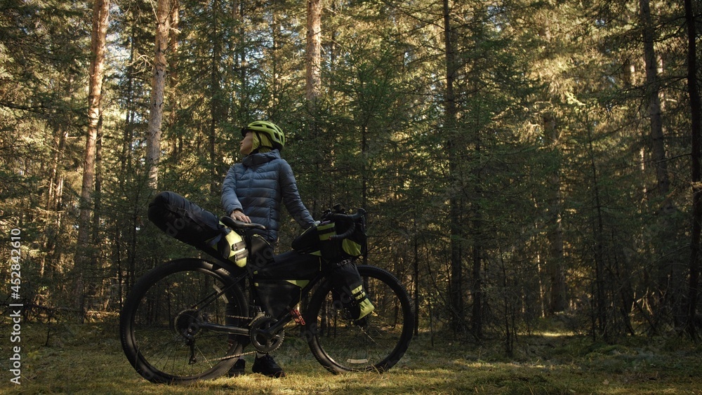 The woman travel on mixed terrain cycle touring with bike bikepacking outdoor. The traveler journey with bicycle bags. Stylish bikepacking, bike, sportswear in green black colors. Magic forest park.